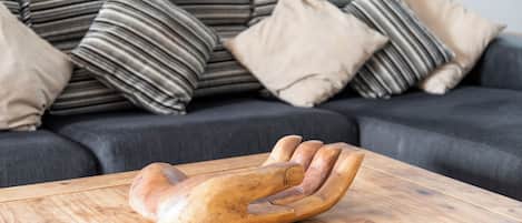 A wooden hand-shaped object on a wooden table in a living room with a dark sofa and striped cushions.