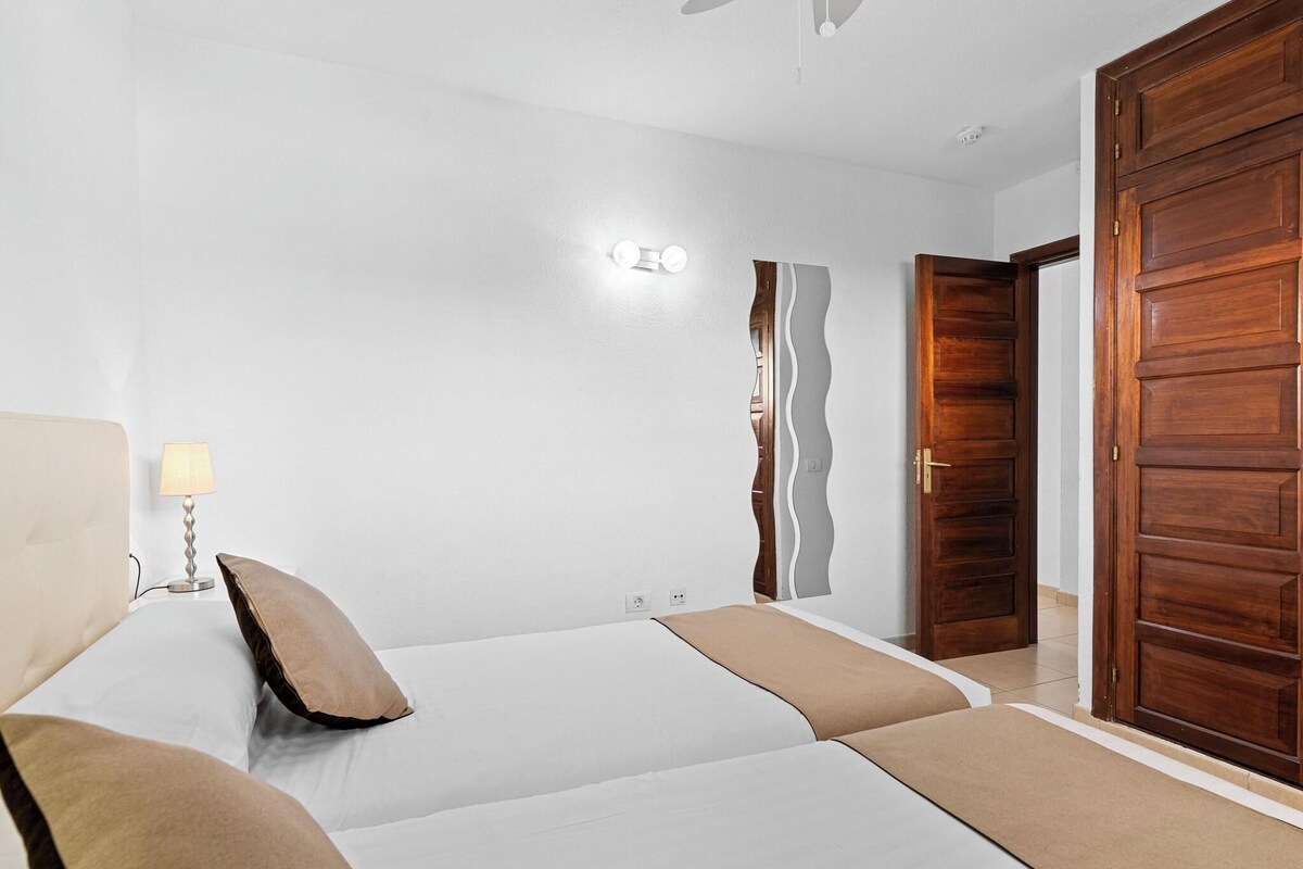 Un dormitorio con cama, lámpara de noche, armario de madera y un aplique en la pared.