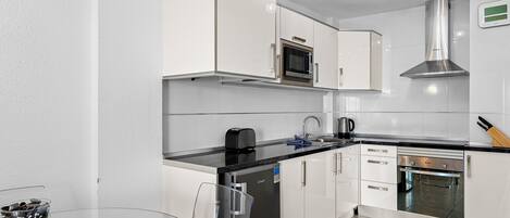 A modern kitchen with white cabinetry, a black countertop, a built-in oven, and a stainless steel range hood.