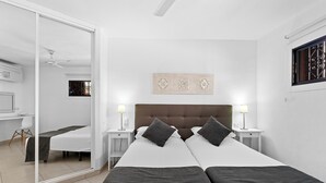 A hotel room with a large bed, two bedside tables, a ceiling fan, and a window with decorative grills. - Paloma Beach Apartments (Arona)