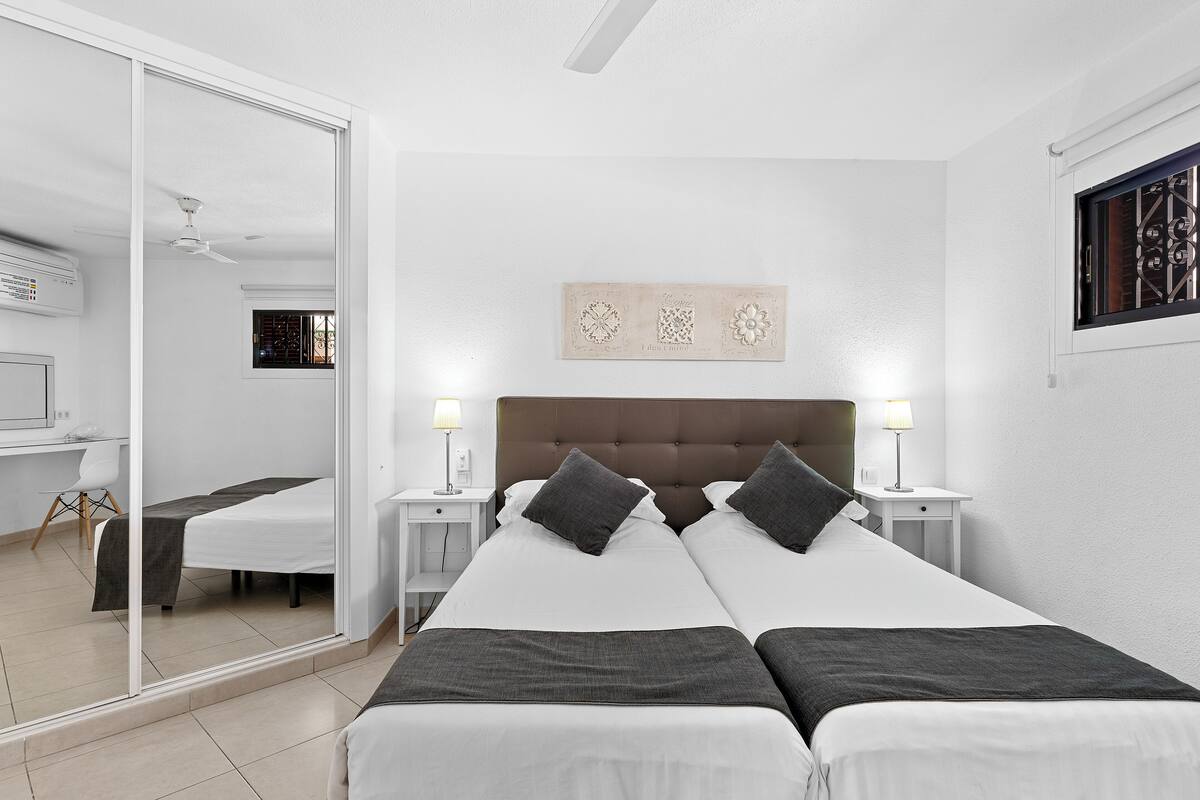 A hotel room with a large bed, two bedside tables, a ceiling fan, and a window with decorative grills.