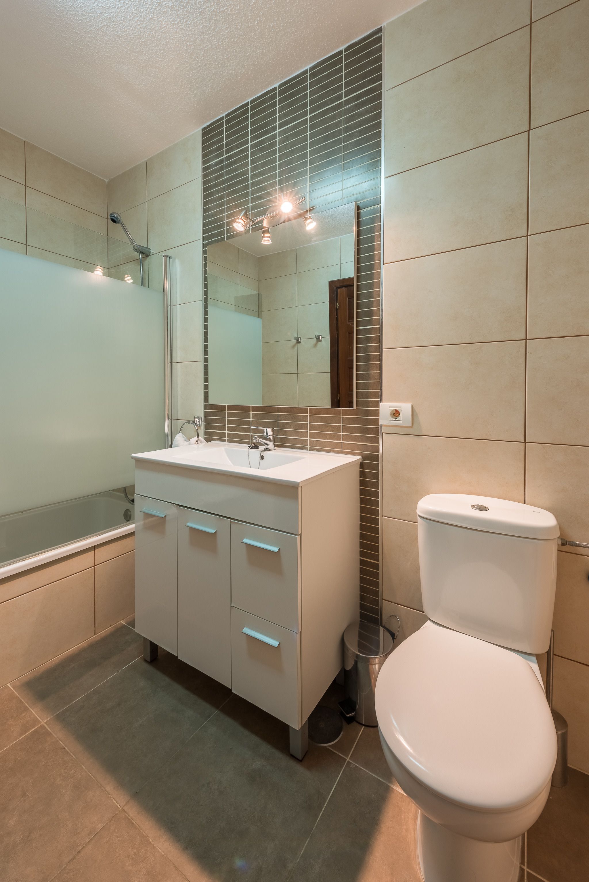 A modern bathroom with a white sink, mirror, and toilet.