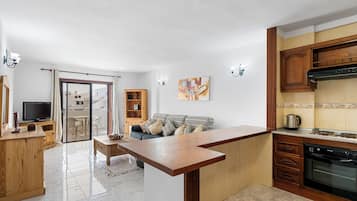 Una cocina moderna con armarios de madera, horno integrado y un comedor con puerta de vidrio que da a un balcón.