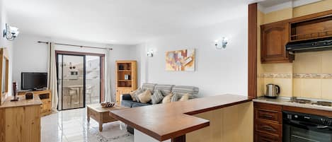 Een moderne keuken met houten kasten, een ingebouwde oven en een eethoek met een glazen deur die leidt naar een balkon.