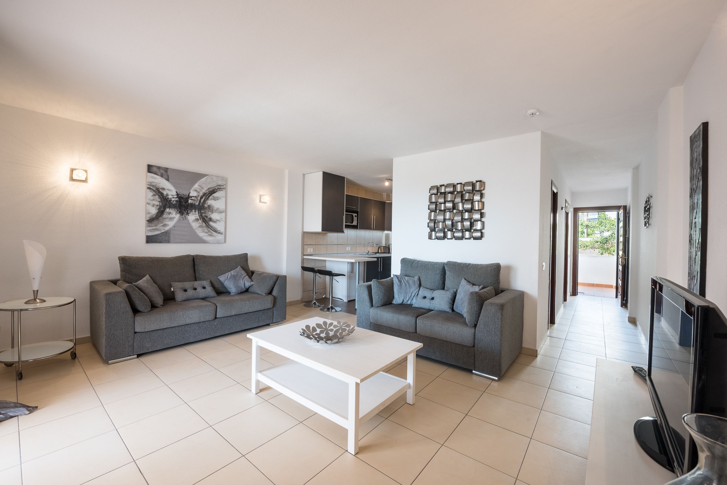 Ein modernes Wohnzimmer mit zwei grauen Sofas, einem weißen Couchtisch und einer Küche im Hintergrund.