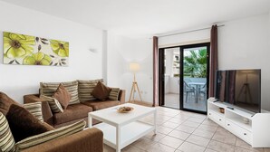 A modern living room with a sofa, coffee table, TV, and a painting on the wall. - Paloma Beach Apartments (Arona)