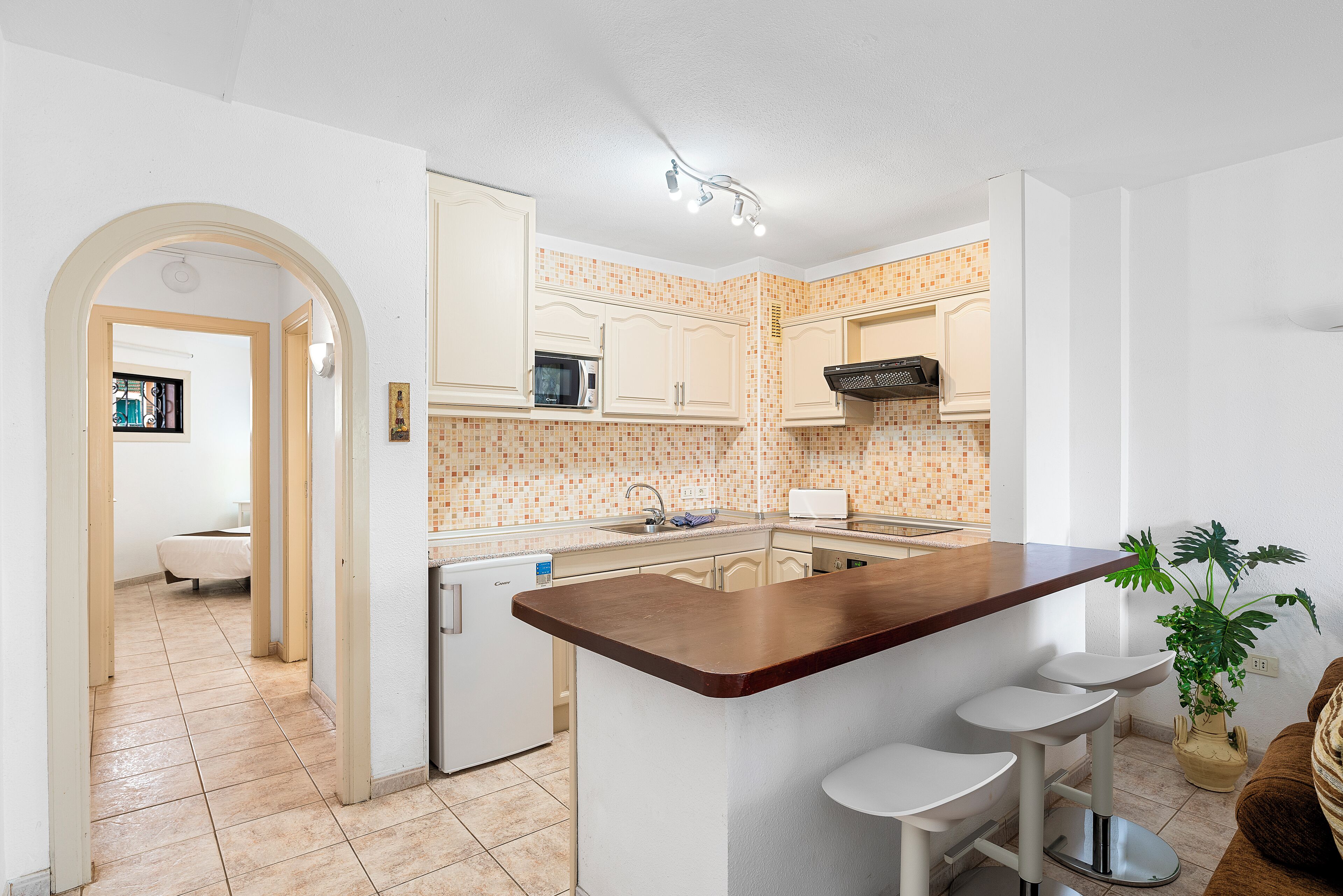 A kitchen with white cabinets, a wooden island with bar stools, a microwave, and a sink.