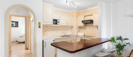 A kitchen with white cabinets, a wooden island with bar stools, a microwave, and a sink.