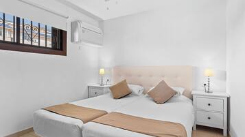 Un llit doble amb dos taulells laterals, cadascun amb una làmpada, en una habitació amb parets blanques i un ventilador de sostre.