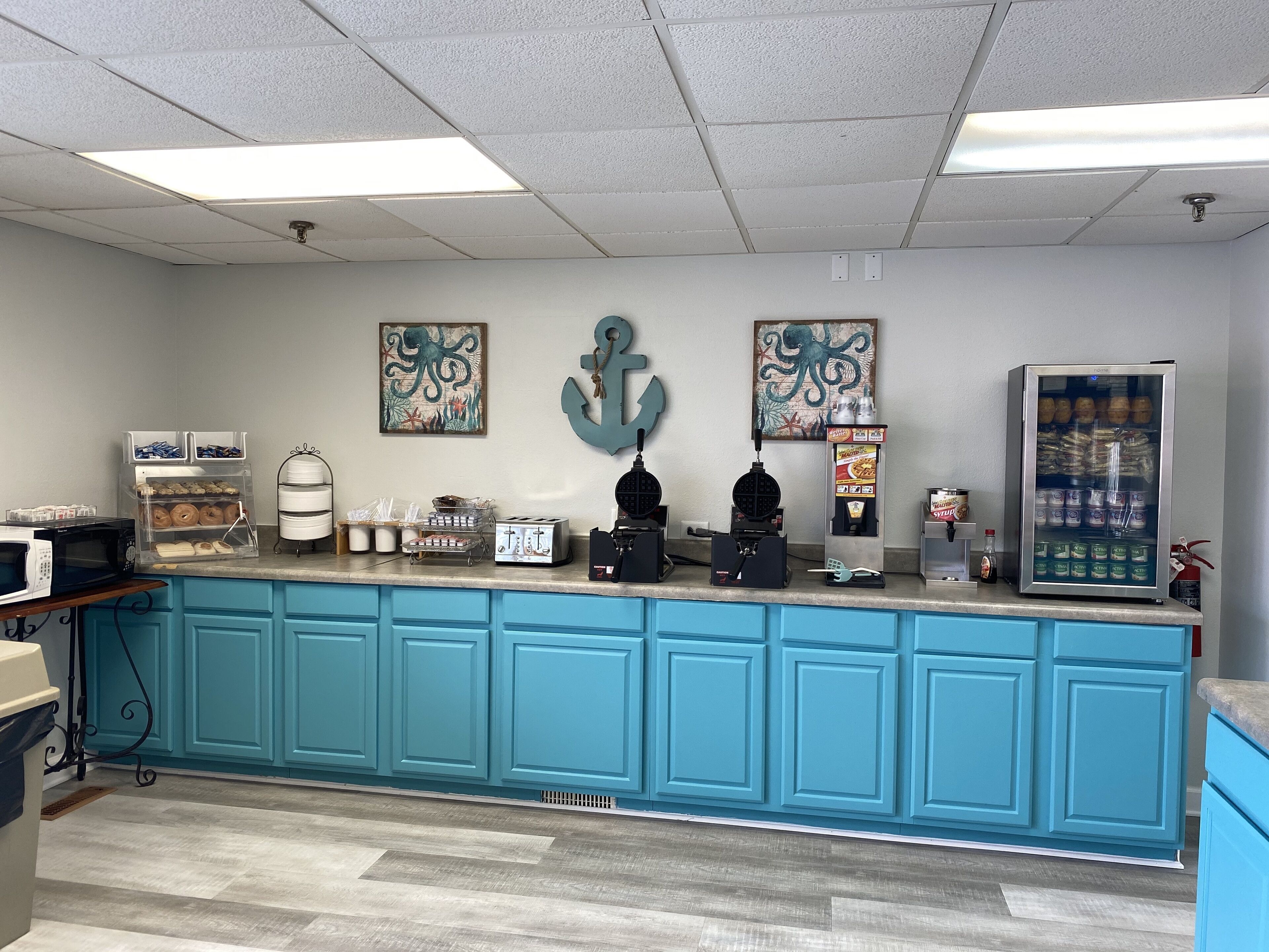 A kitchen area with teal cabinets, a microwave, toaster, waffle maker, and a refrigerator.