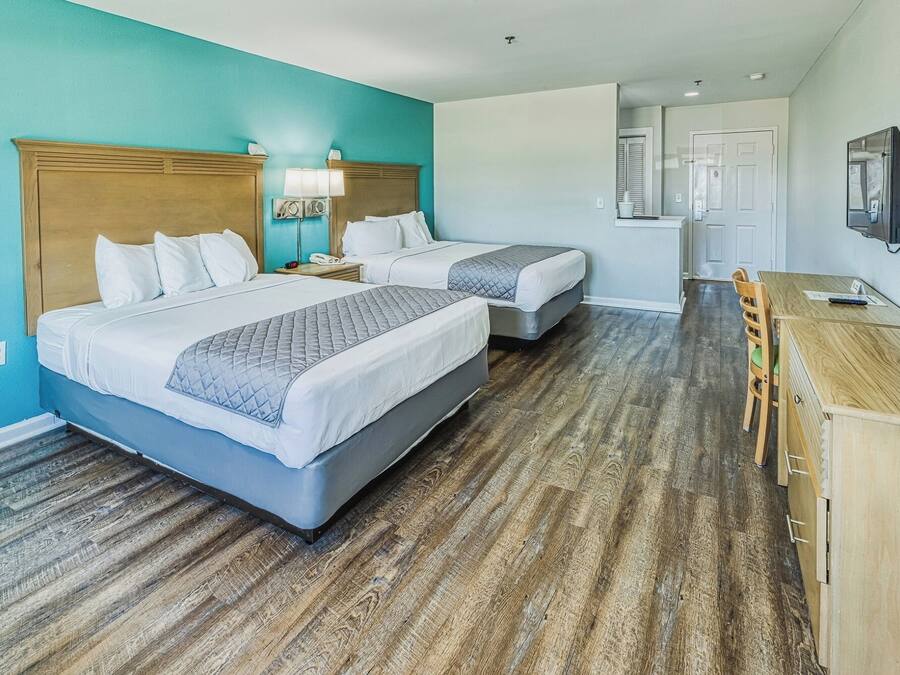 Habitación de hotel con dos camas, un escritorio, una silla, un televisor y una puerta que da a un baño.