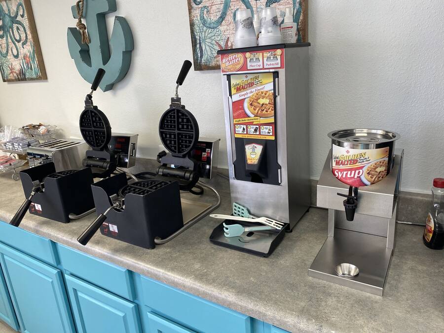 A kitchen counter with waffle makers, a syrup dispenser, and a waffle maker box.
