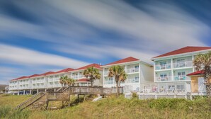 A beachfront hotel with multiple-story buildings, balconies, and a wooden walkway leading to the beach. - The Islander Inn (Ocean Isle Beach)