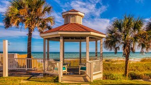 A gazebo with a red roof and white walls, surrounded by palm trees and overlooking the ocean. - The Islander Inn (Ocean Isle Beach)