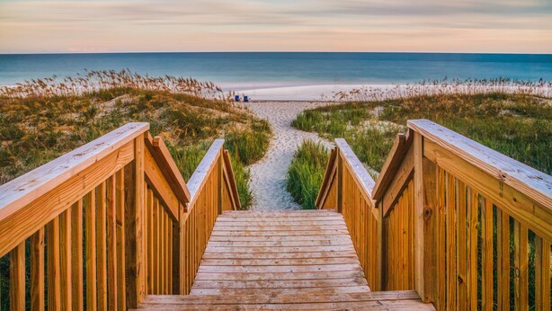 A wooden staircase leading to a beach with a clear view of the ocean. - The Islander Inn (Ocean Isle Beach)
