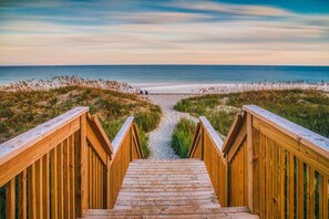 A wooden staircase leading to a beach with a clear view of the ocean. - The Islander Inn (Ocean Isle Beach)