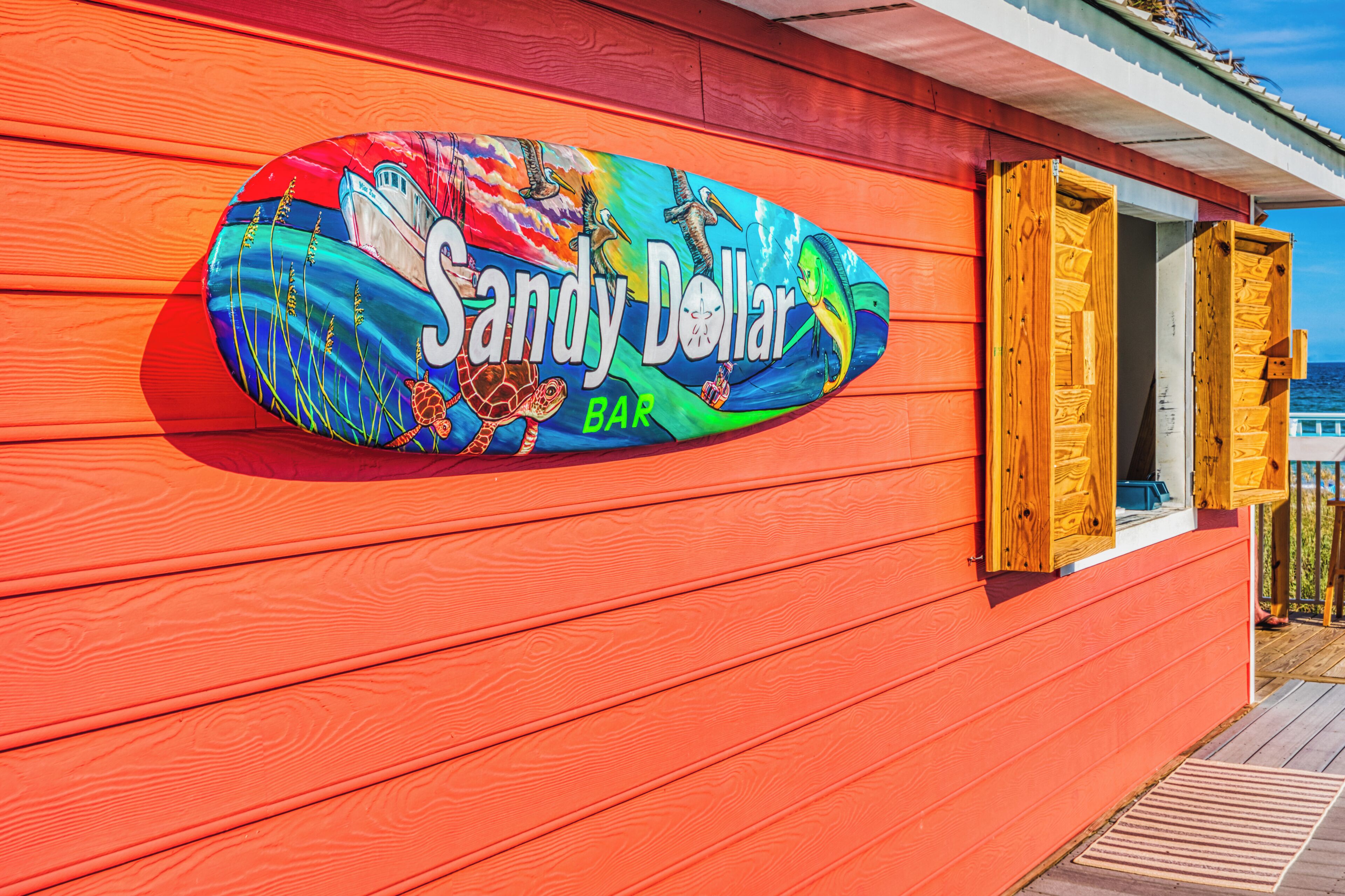 A colorful sign for Sandy Dollar Bar on a wooden building.