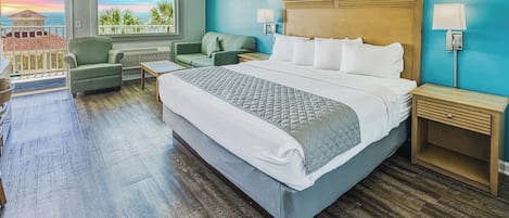 Habitación de hotel con una cama grande, dos mesitas de noche, un sofá, una silla y vistas al océano.