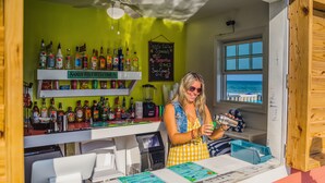 A bar with a green wall, a wooden counter, and a view of the ocean through a window. - The Islander Inn (Ocean Isle Beach)