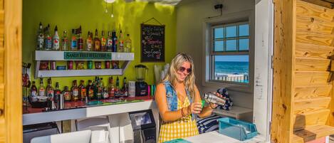 Un bar con una pared verde, una barra de madera y vista al océano a través de una ventana.
