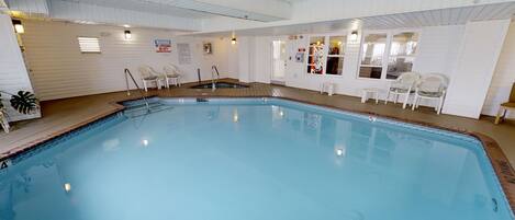 An indoor swimming pool with a wooden deck, white walls, and a lifeguard warning sign.