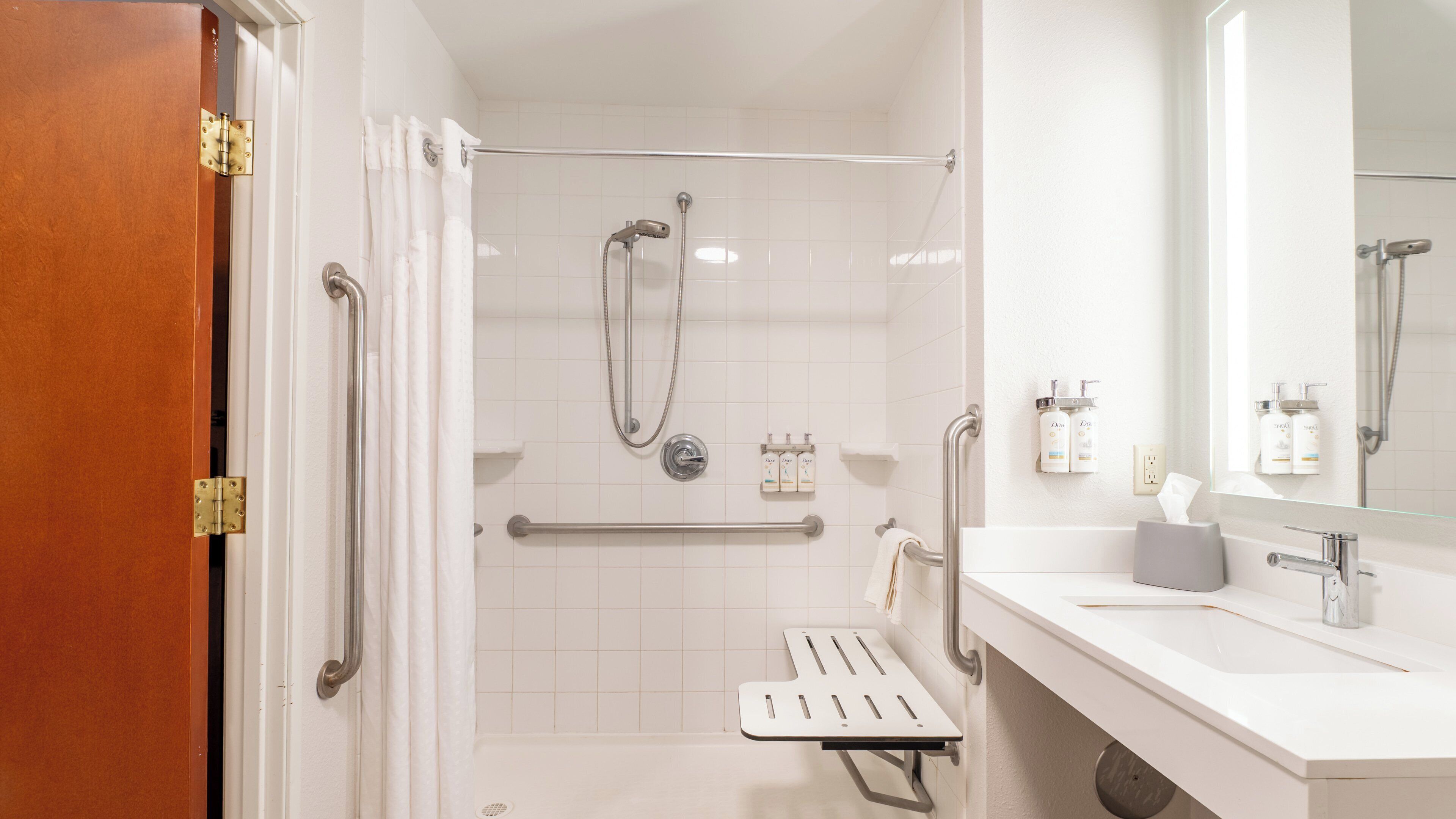 Un baño moderno con ducha, barras de apoyo, lavabo y espejo.