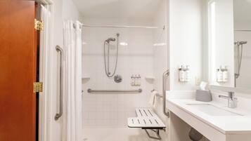 Un baño moderno con ducha, barras de apoyo, lavabo y espejo.