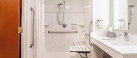 A bathroom with a shower, grab bars, a sink, and a mirror.