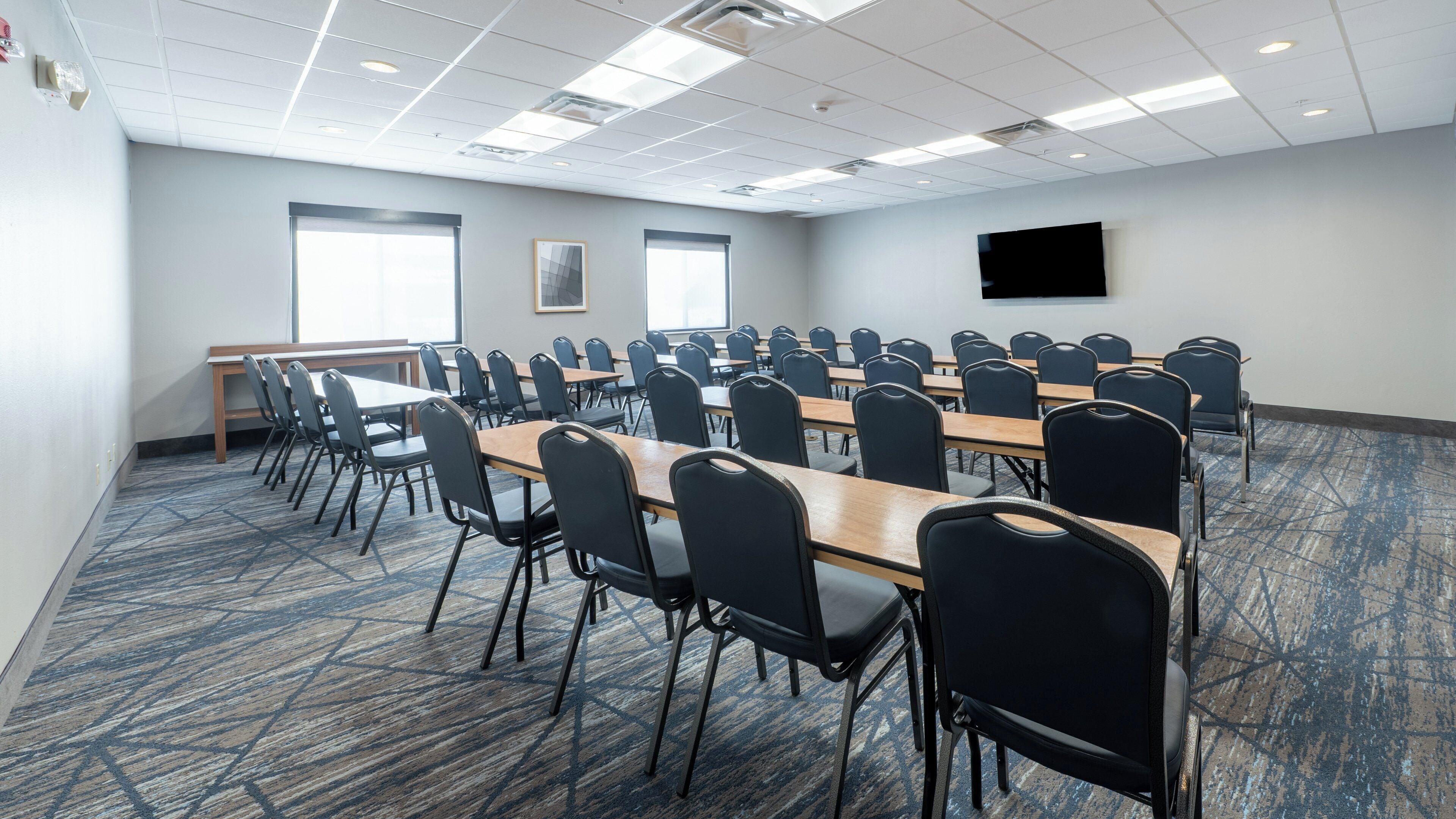 A conference room with multiple tables and chairs, large windows, and a flat-screen TV on the wall.