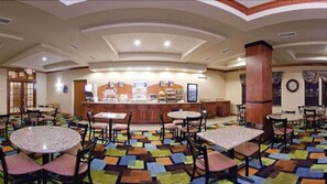 A hotel lobby with multiple round tables and chairs, a central counter with a cash register, and a patterned carpet. - Holiday Inn Express Hotel & Suites ANDERSON NORTH by IHG (Anderson)