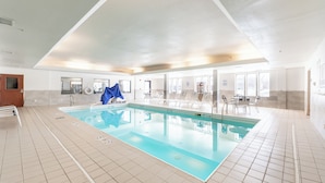 Ein großer, überdachter Schwimmbereich mit klarem Wasser, umgeben von gefliesten Wänden und einer hohen Decke.