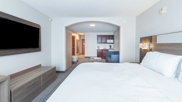 Ein Hotelzimmer mit einem großen Bett, einem an der Wand montierten Fernseher, einem Schreibtisch und einer Küchenzeile.