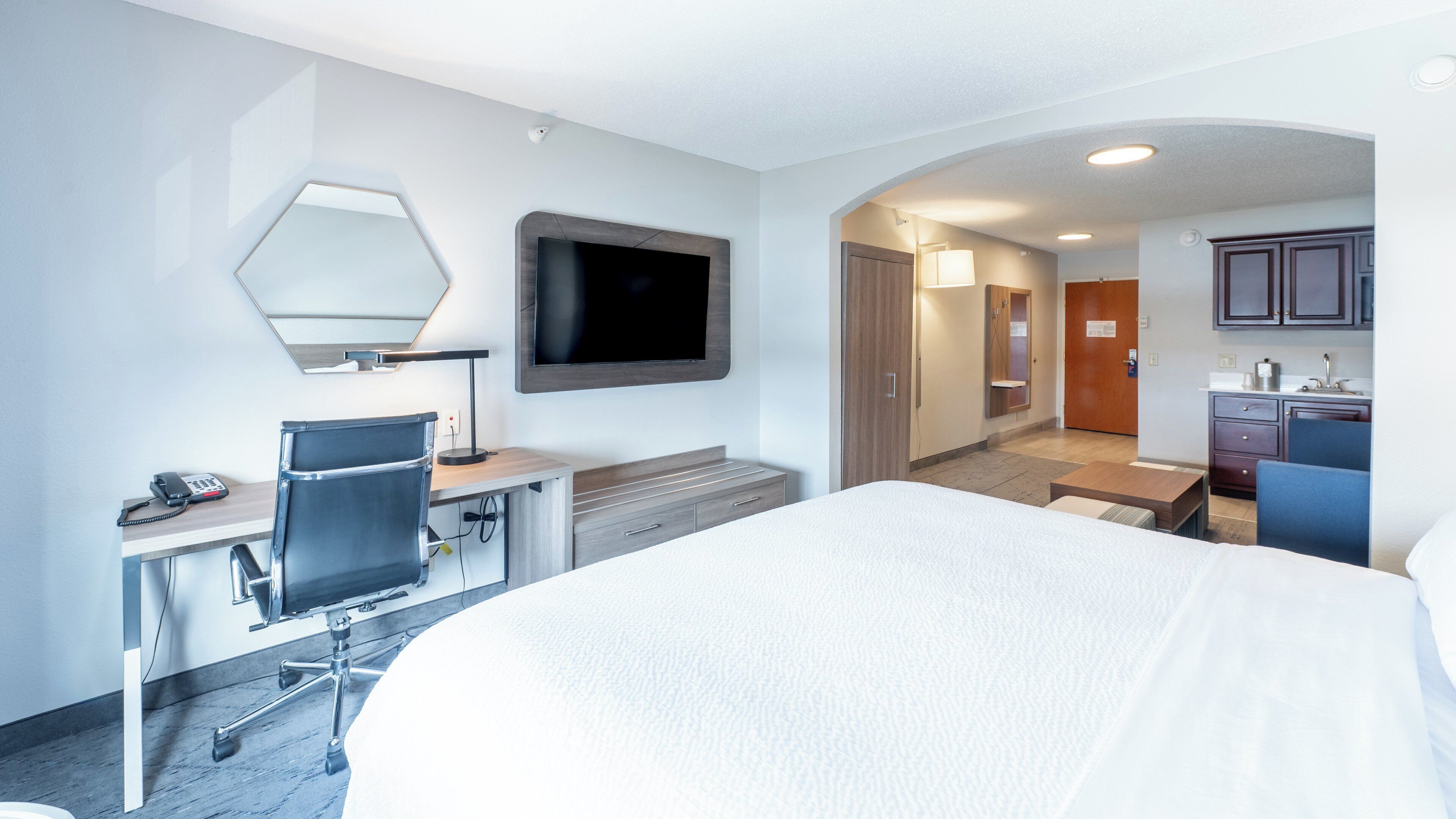 Habitación de hotel con cama, escritorio, silla, televisor y kitchenette.