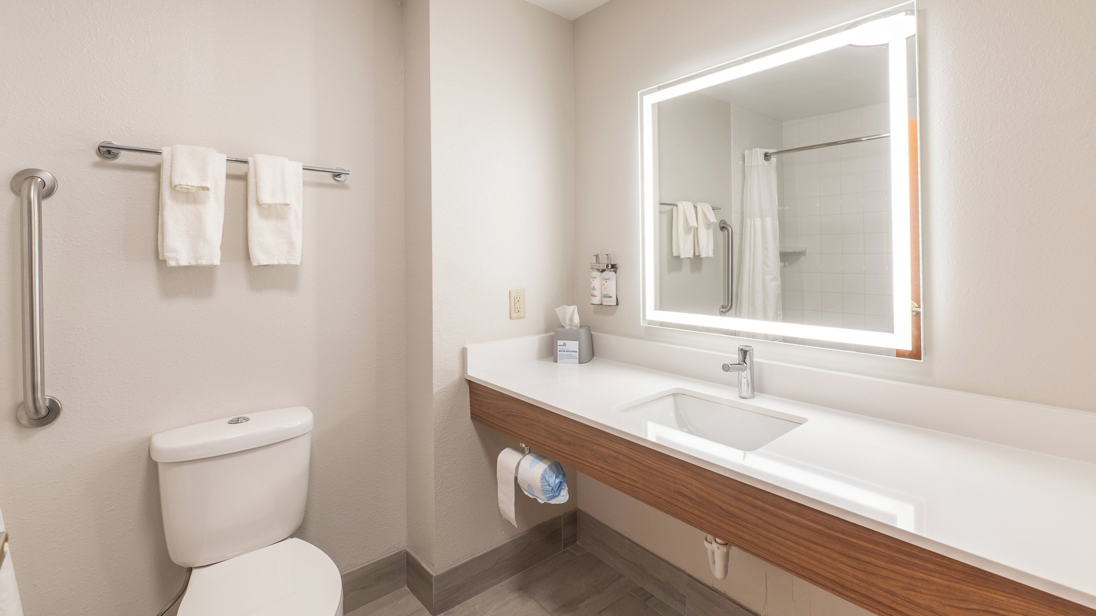 Un baño moderno con inodoro, lavamanos, espejo y toallero.