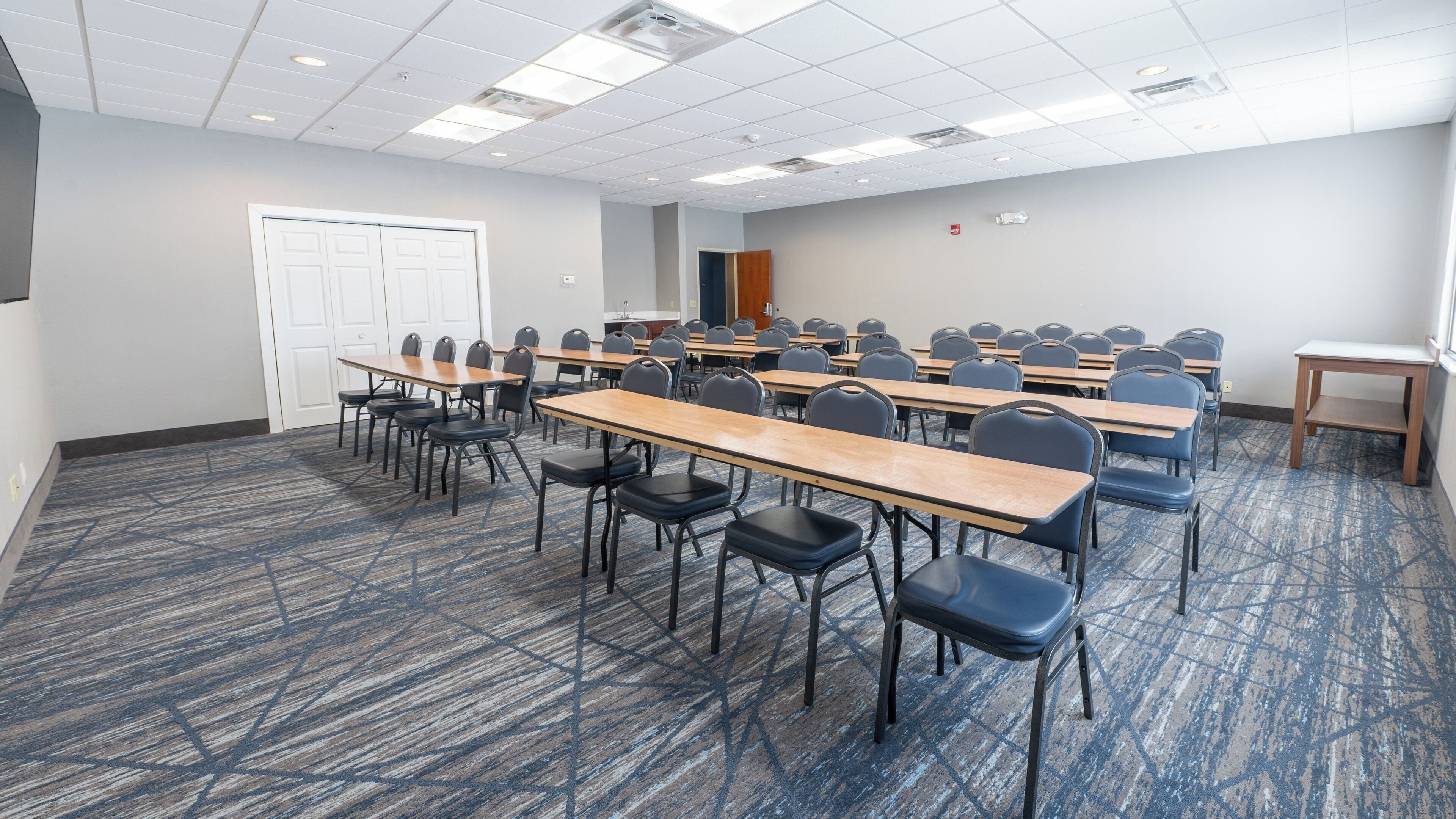 A conference room with multiple tables and chairs, a door, and a small table with a lamp.