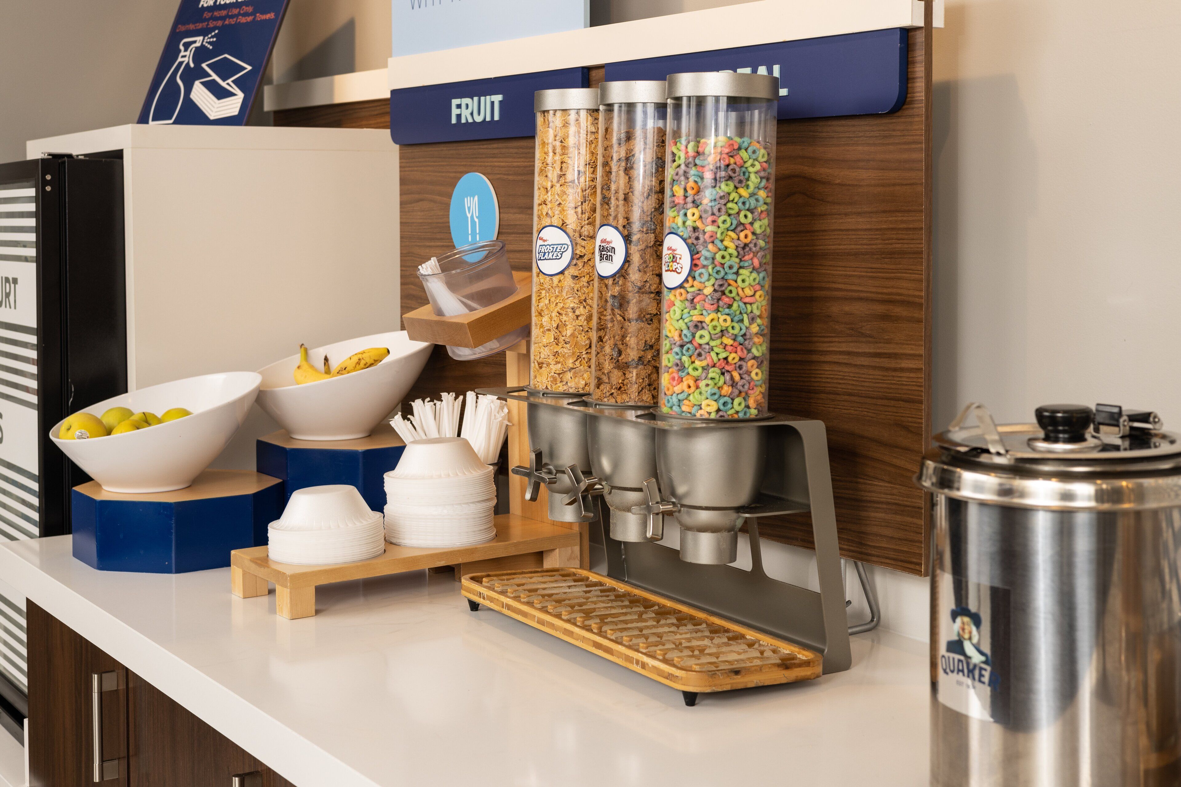 Un comptoir pour le petit-déjeuner avec des bols de fruits, des distributeurs de céréales et une machine à café.
