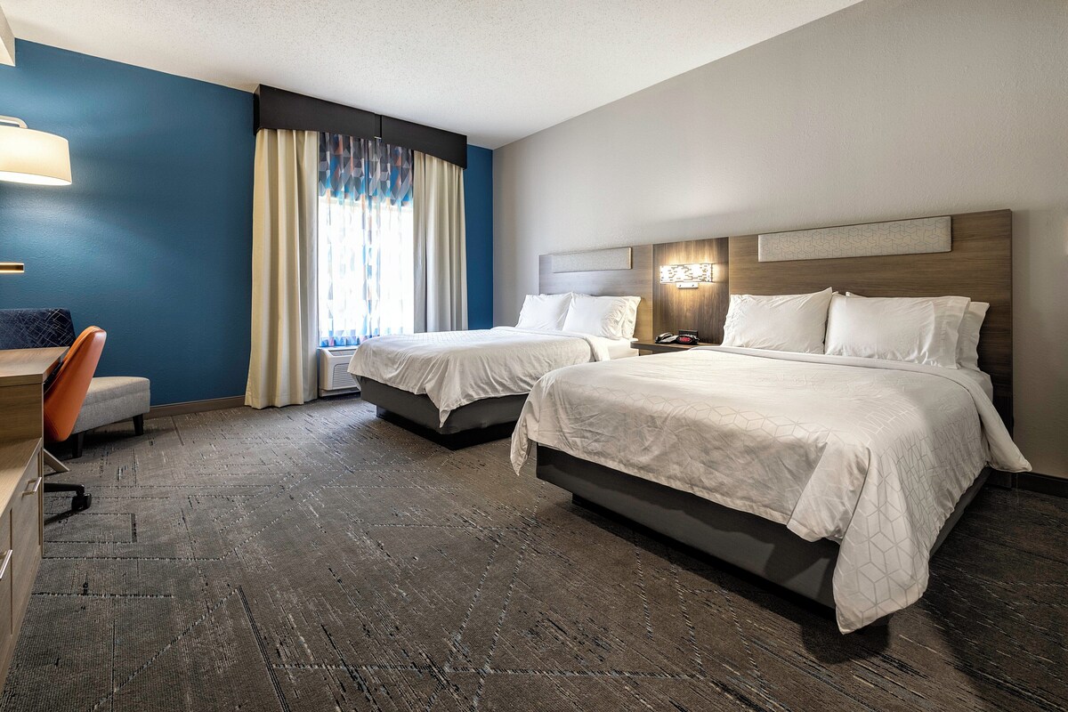 A hotel room with two beds, a desk, and a chair.
