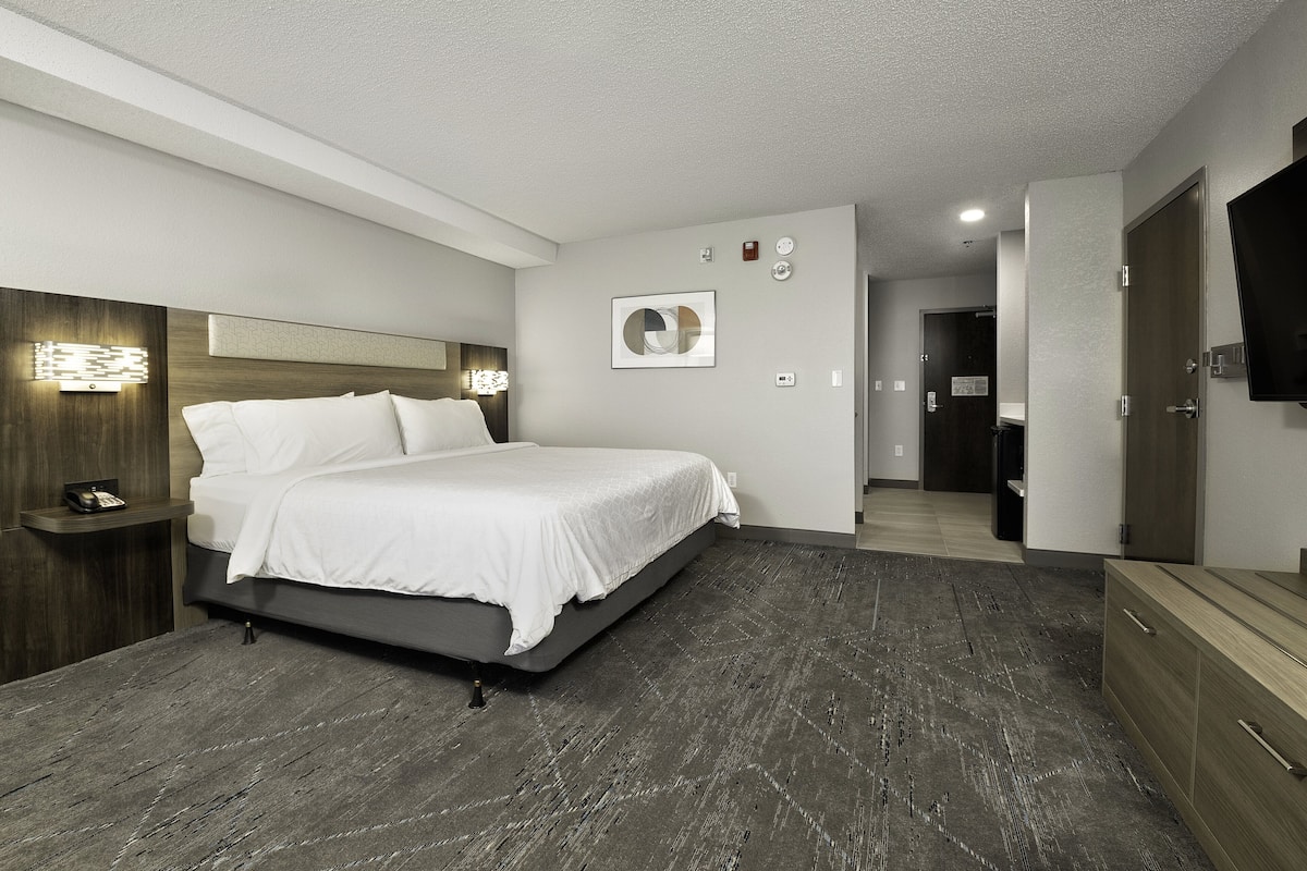 A modern hotel room with a large bed, a bedside table, a flat-screen TV, and a wooden dresser.