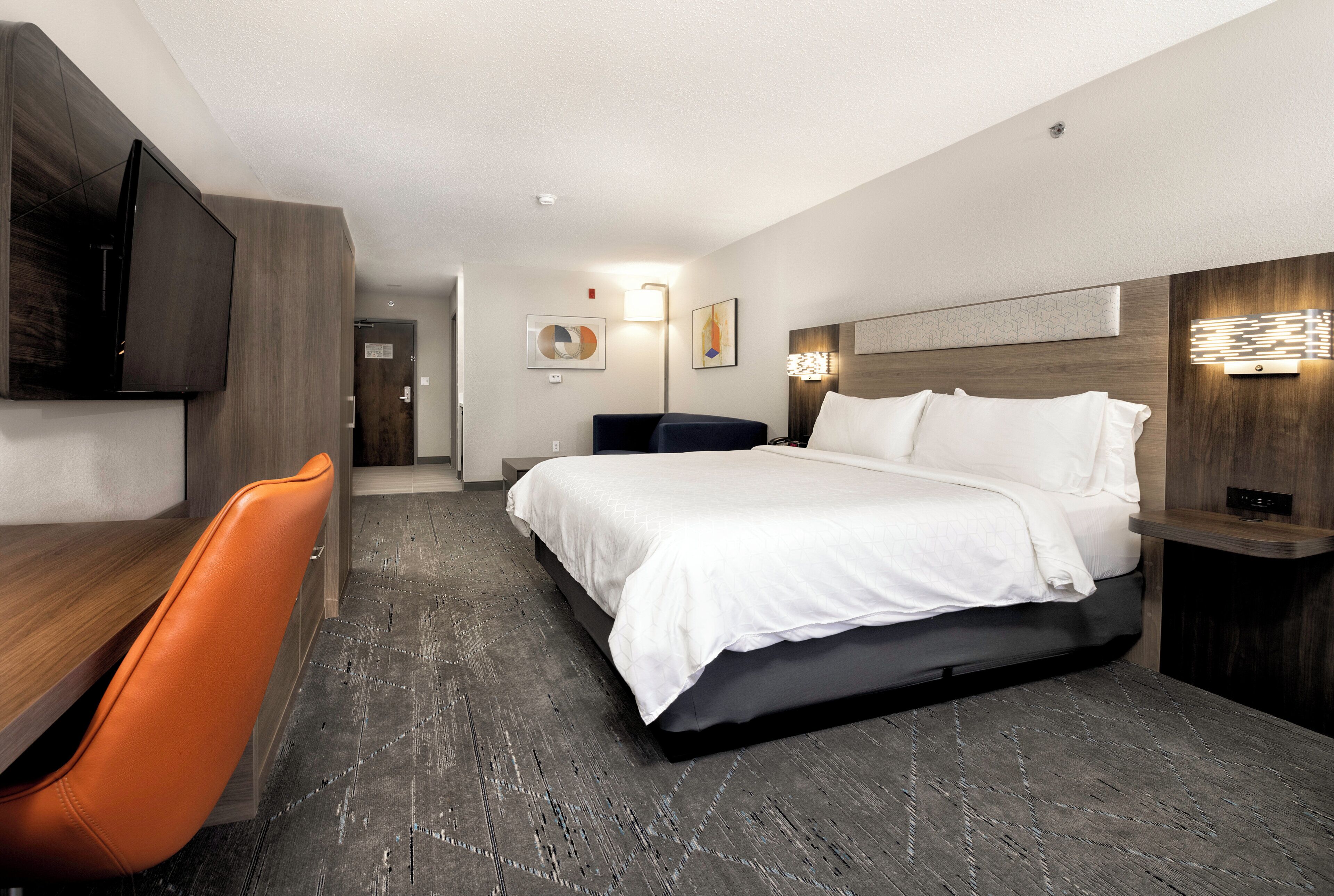 A hotel room with a bed, a desk, a chair, and a TV.
