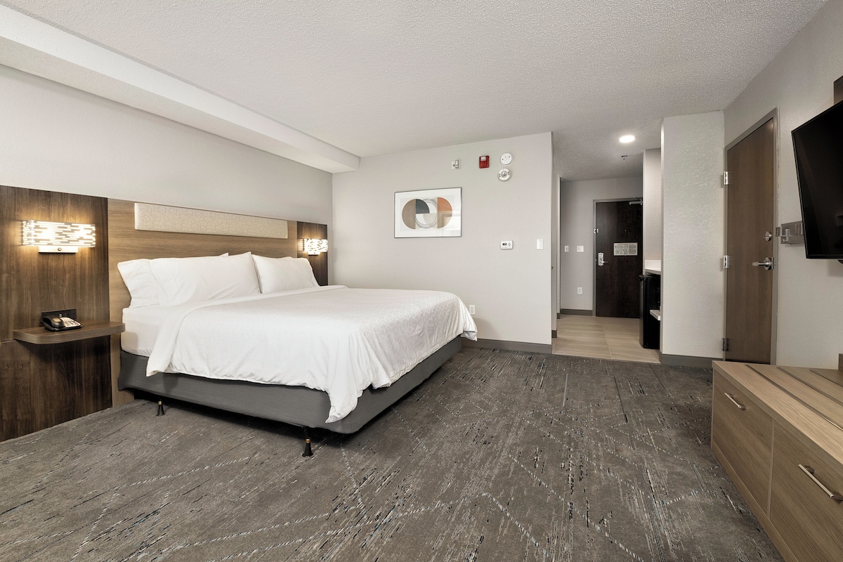 A modern hotel room with a large bed, a bedside table, a flat-screen TV, and a wooden dresser.