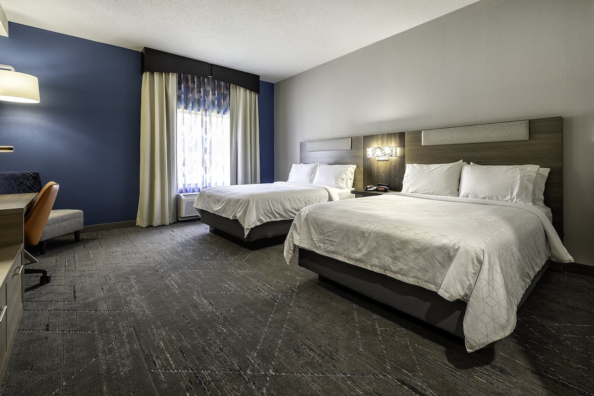 A hotel room with two beds, a desk, and a chair.