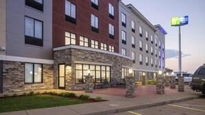 A modern hotel with a stone facade, multiple windows, outdoor seating, and a visible sign for the Holiday Inn Express & Suites.