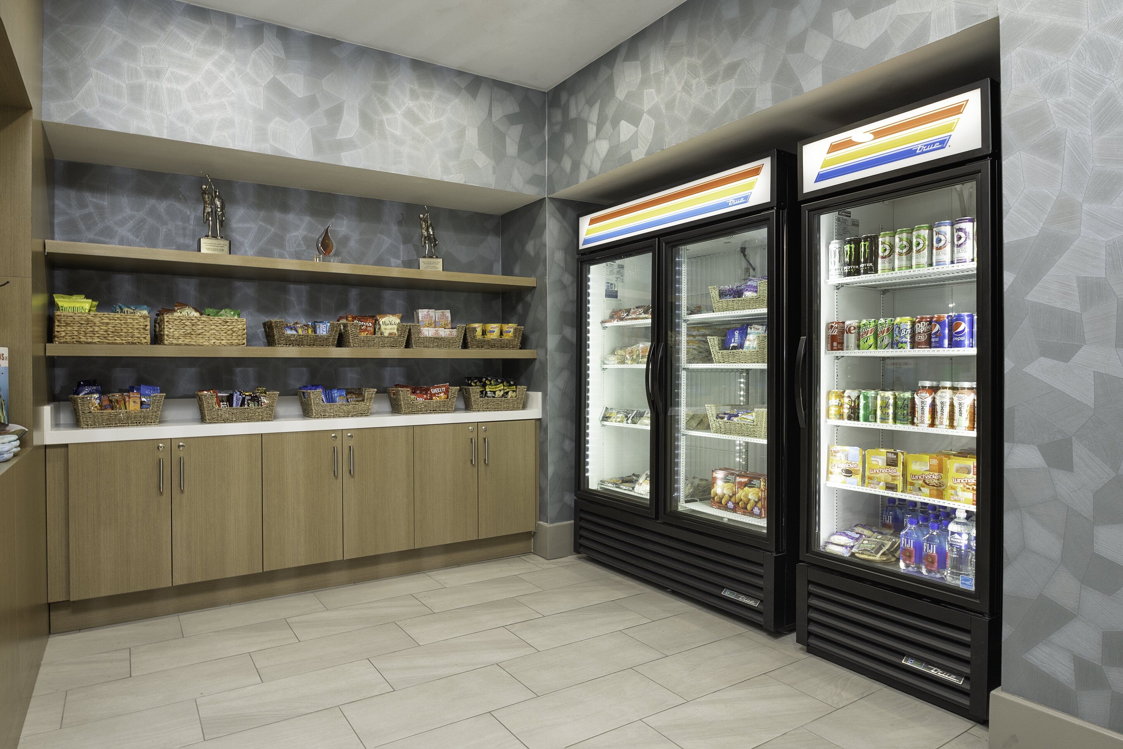 Un bar de aperitivos limpio y ordenado, con estantes llenos de diversas opciones y una vitrina refrigerada con bebidas.