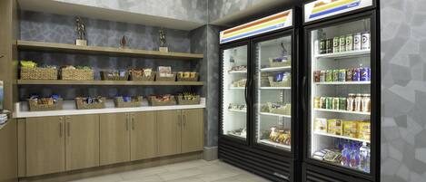Un bar de aperitivos limpio y ordenado, con estantes llenos de diversas opciones y una vitrina refrigerada con bebidas.