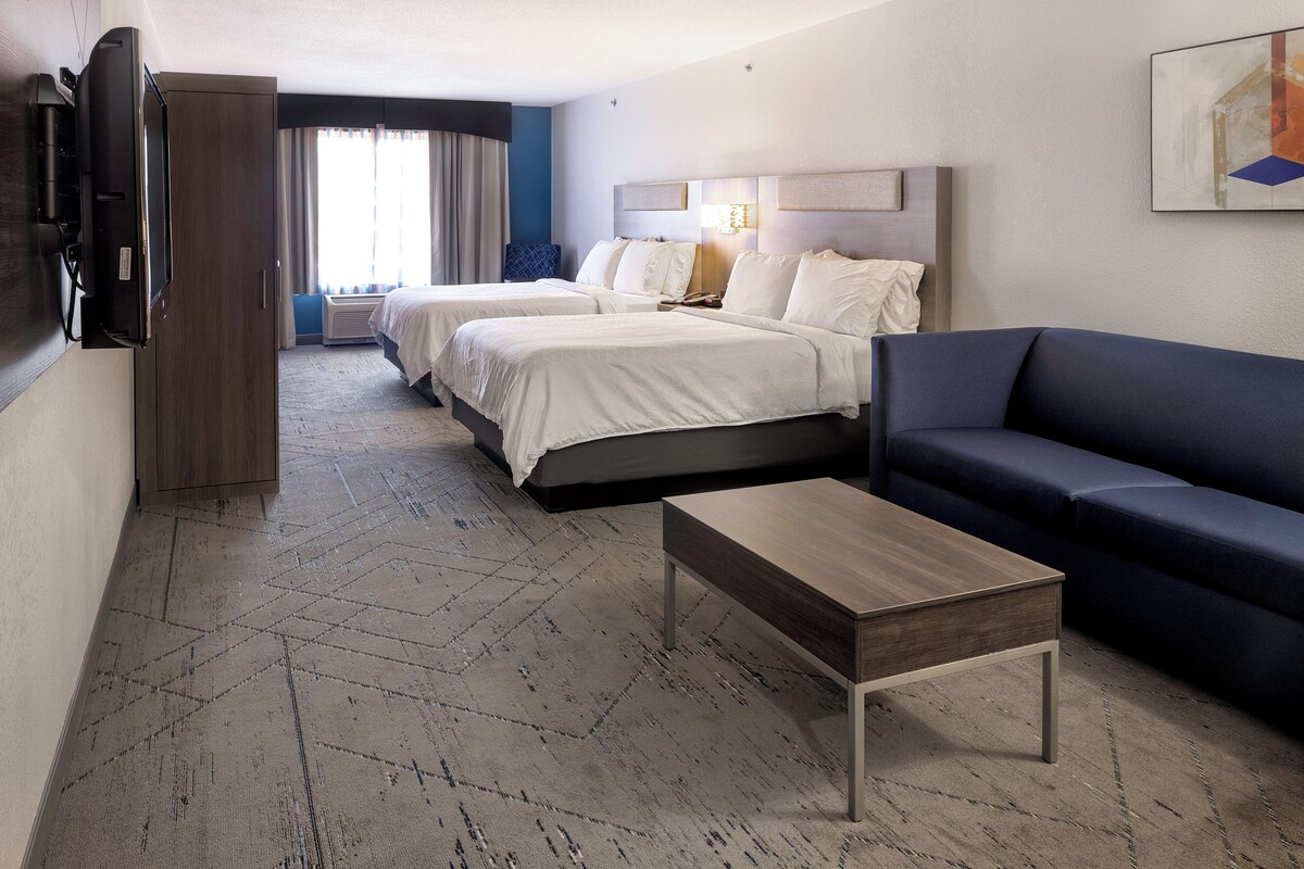 A hotel room with two beds, a sofa, a TV, and a coffee table.