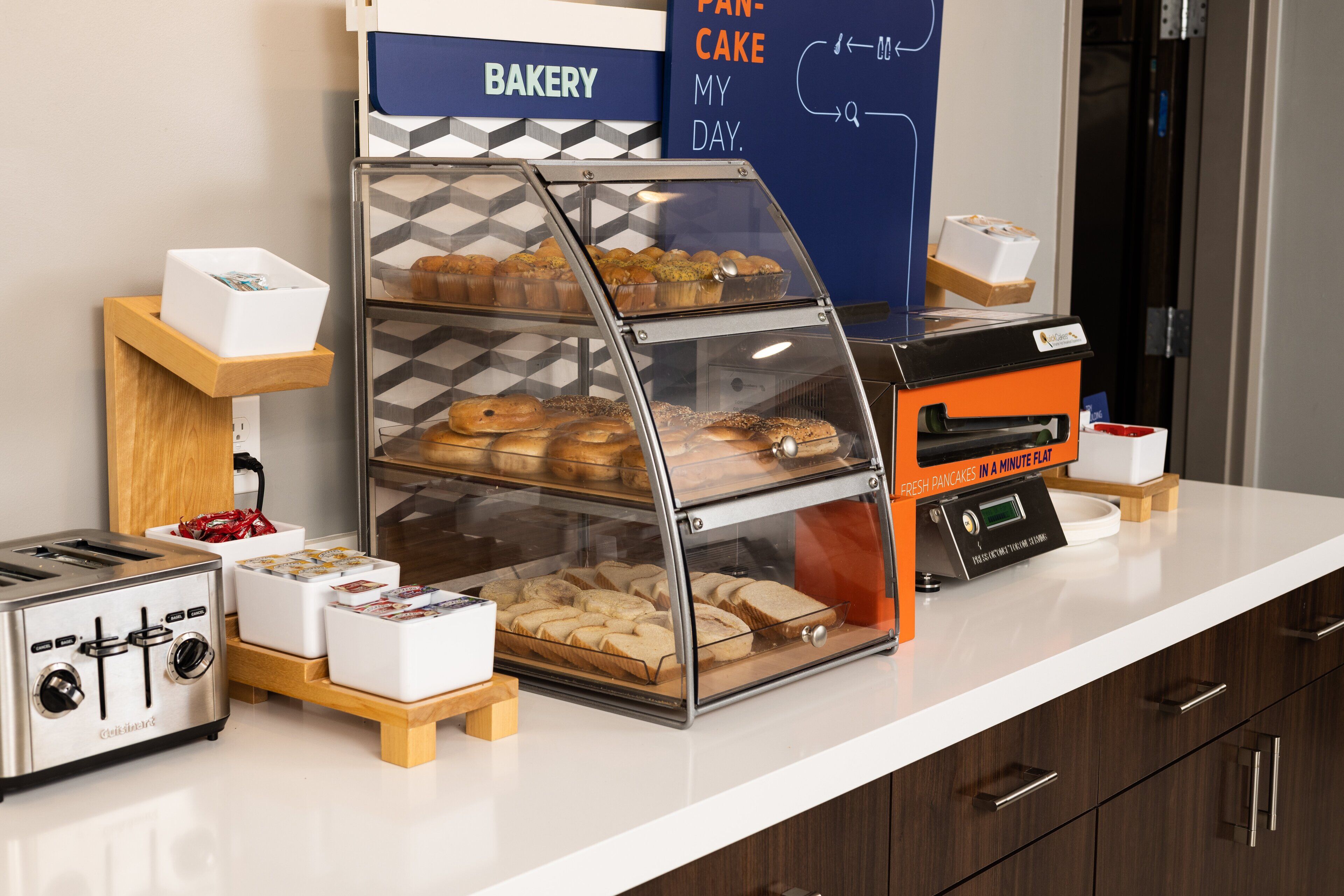 A bakery display with various baked goods, a toaster, and a sign that reads "PANCAKE MY DAY."
