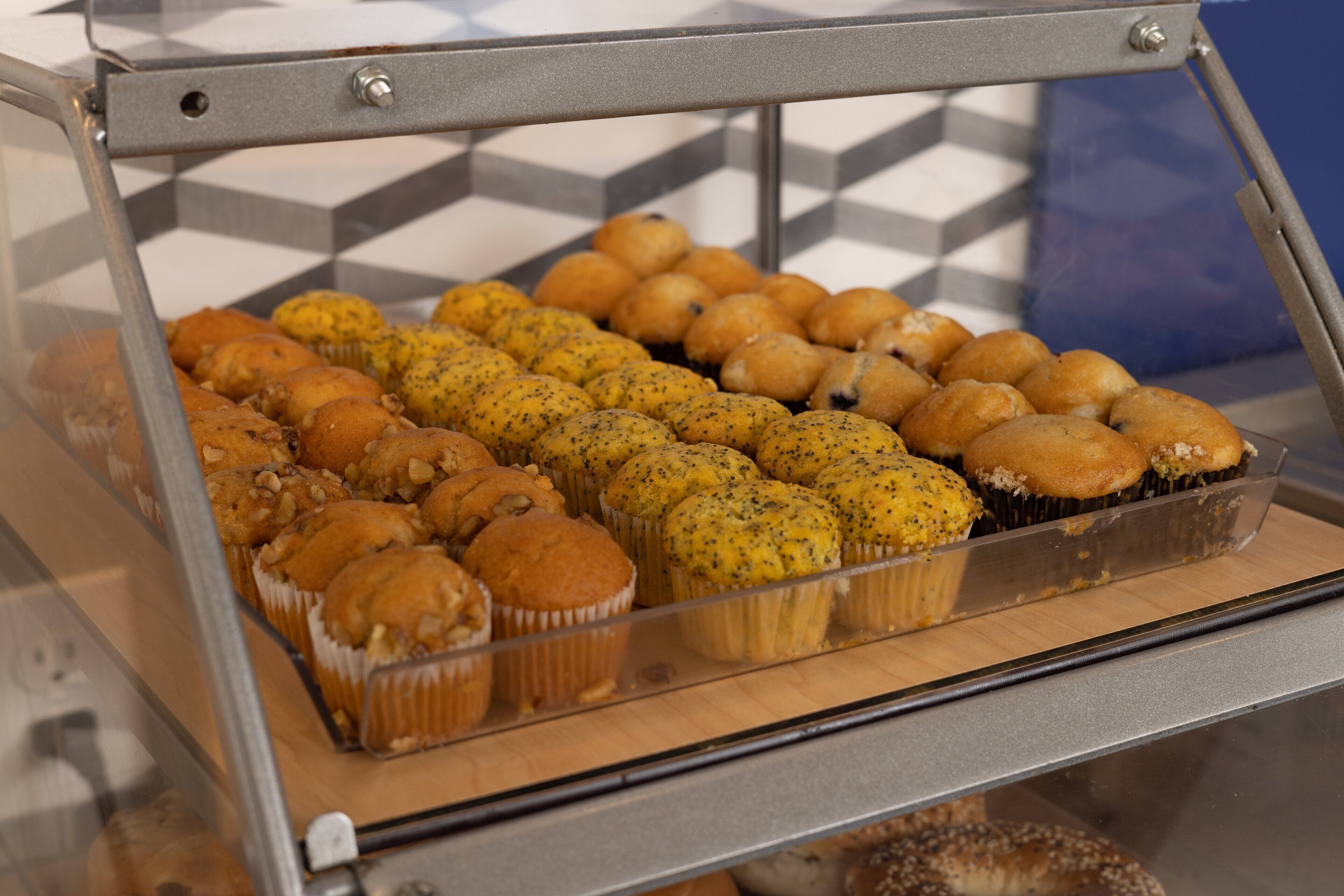 A bakery display case with various baked goods, including muffins and poppy seed buns.