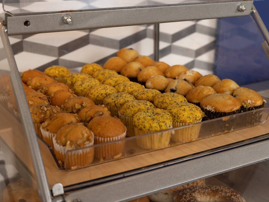 A bakery display case with various baked goods, including muffins and poppy seed buns.