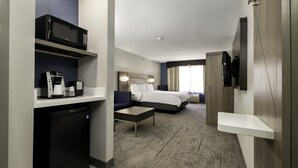 A hotel room with a bed, a desk, a microwave, a coffee maker, and a TV mounted on the wall.