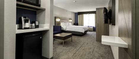 A hotel room with a bed, a desk, a microwave, a coffee maker, and a TV mounted on the wall.